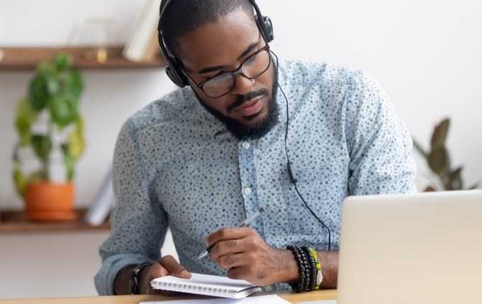 A man takes notes while watching a computer screen.