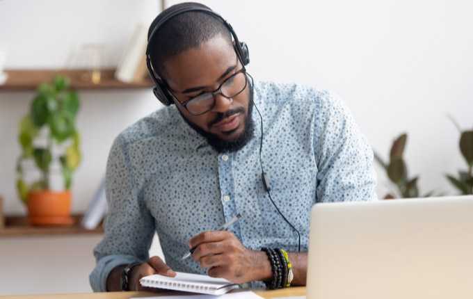 A man takes notes while watching a computer screen.
